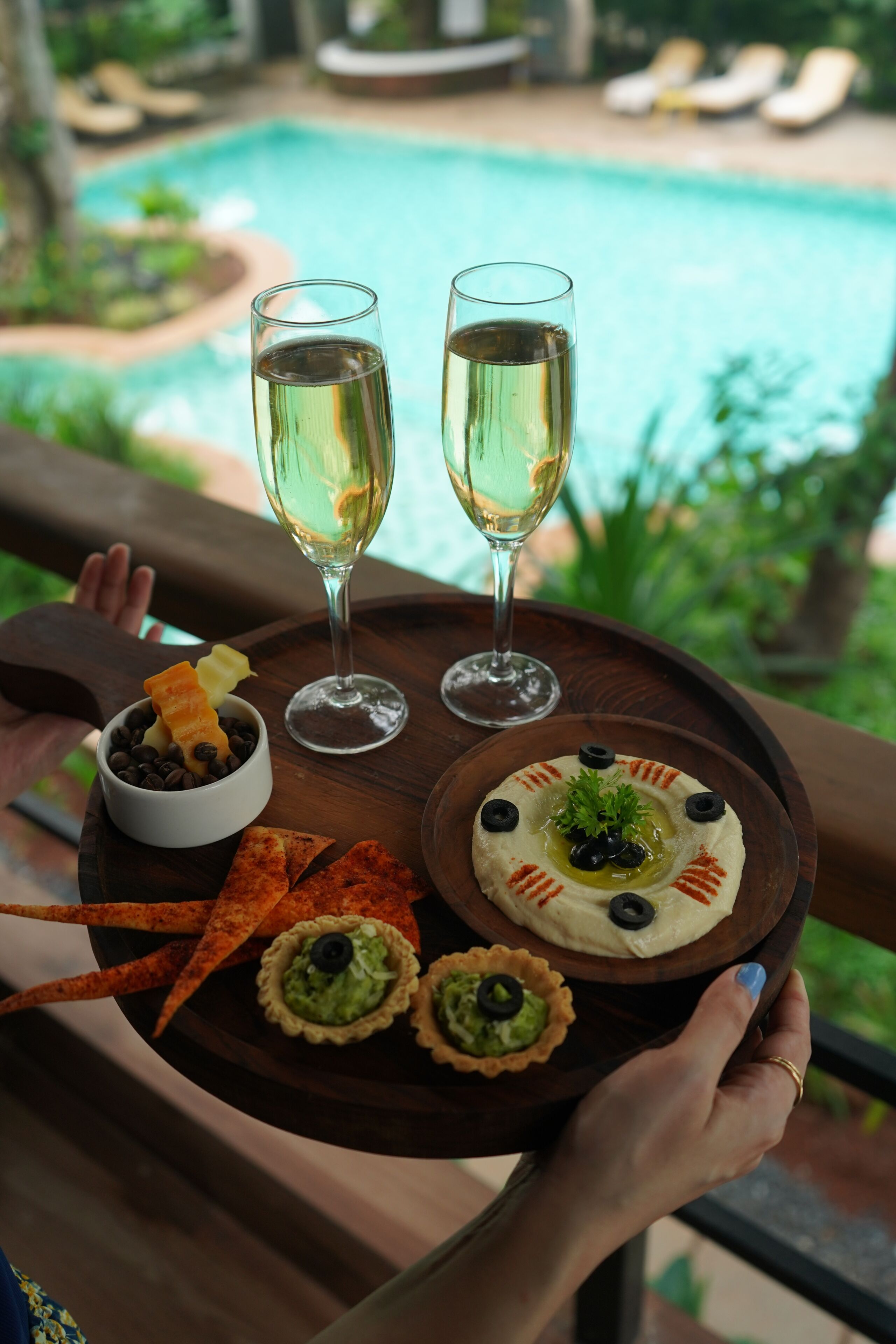 A tray with food and drinks, a pool, and greenery in the background.