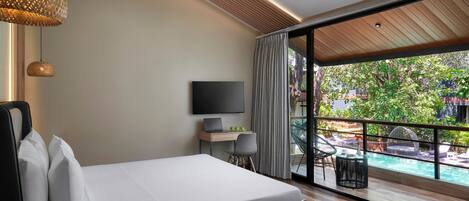 A modern hotel room with a bed, a desk with a laptop, a TV, and a view of a swimming pool.
