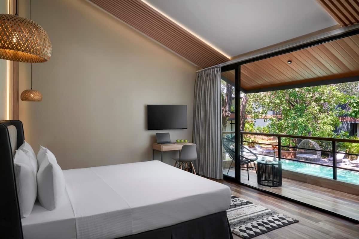Una habitación de hotel moderna con una cama grande, televisión, escritorio y vista a una piscina al aire libre.