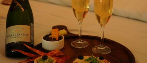 Una cama con sábanas blancas, una botella de Moët & Chandon, dos copas de champán y una bandeja de madera con aperitivos.