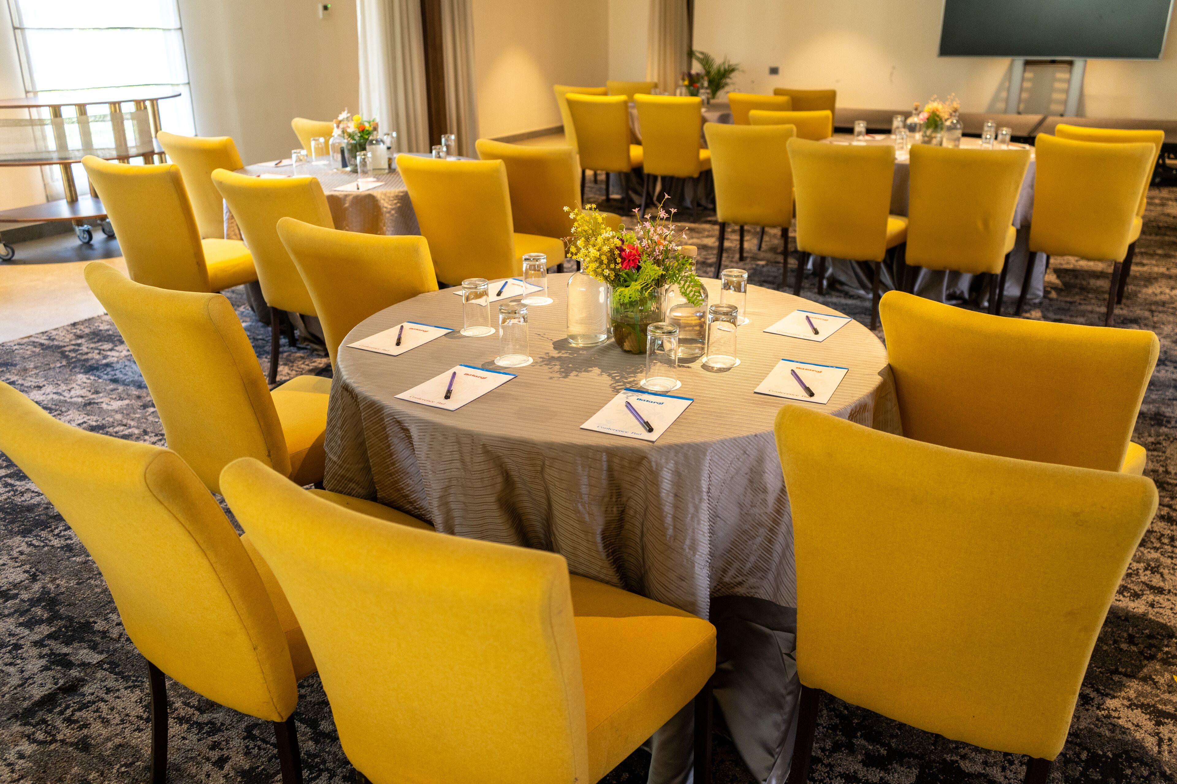 Une salle de conférence avec des chaises et des tables jaunes, équipée de porte-noms, de stylos et de verres.