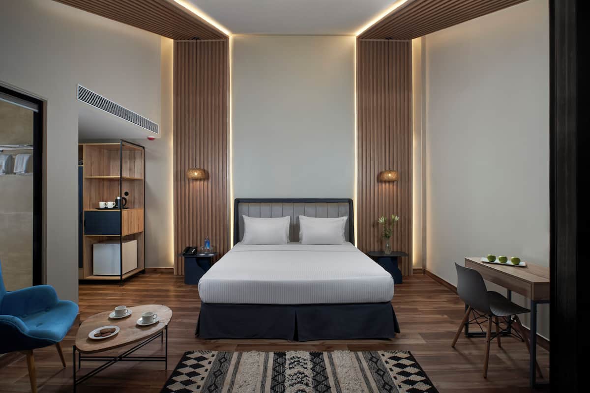 Una habitación de hotel moderna con una cama grande, un escritorio, una silla, una mesita de centro y un armario.