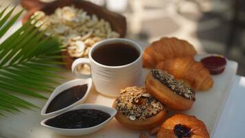 Un desayuno con cruasanes, granola, café y mermelada.