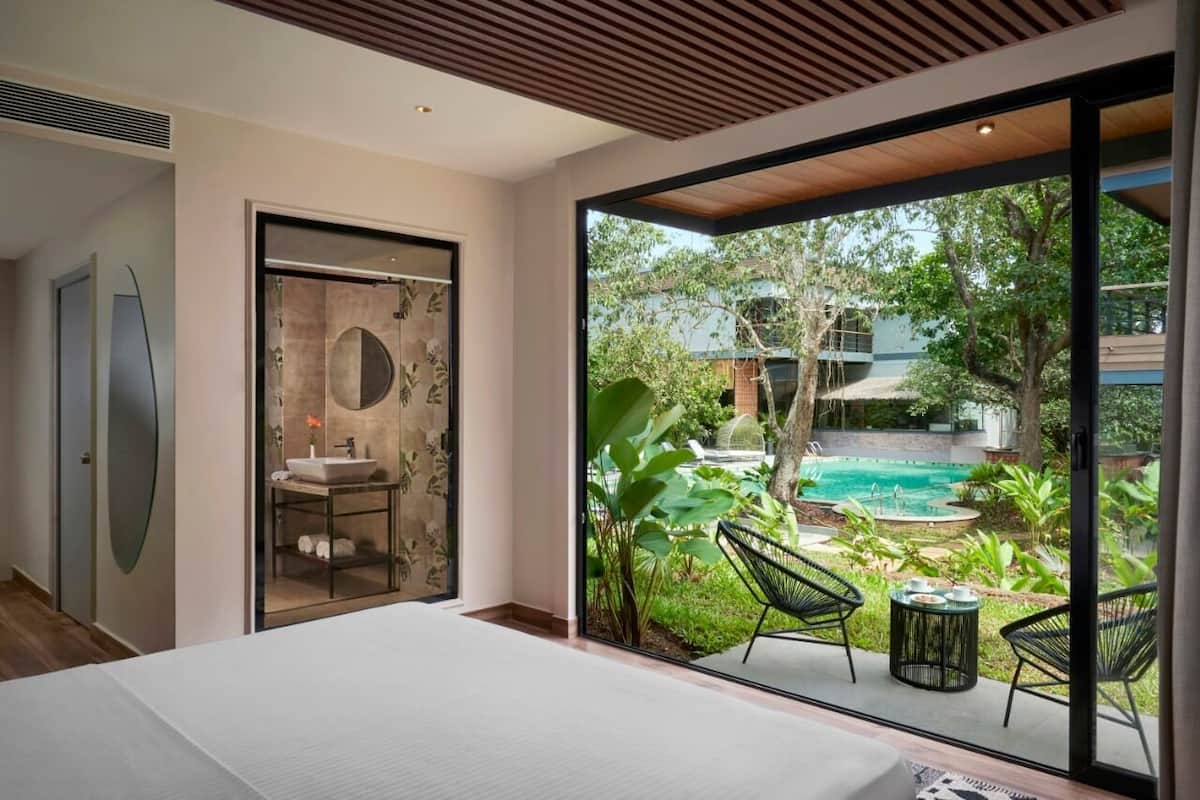 Un dormitorio moderno con una cama grande, un baño con espejo circular y vistas a una piscina al aire libre.