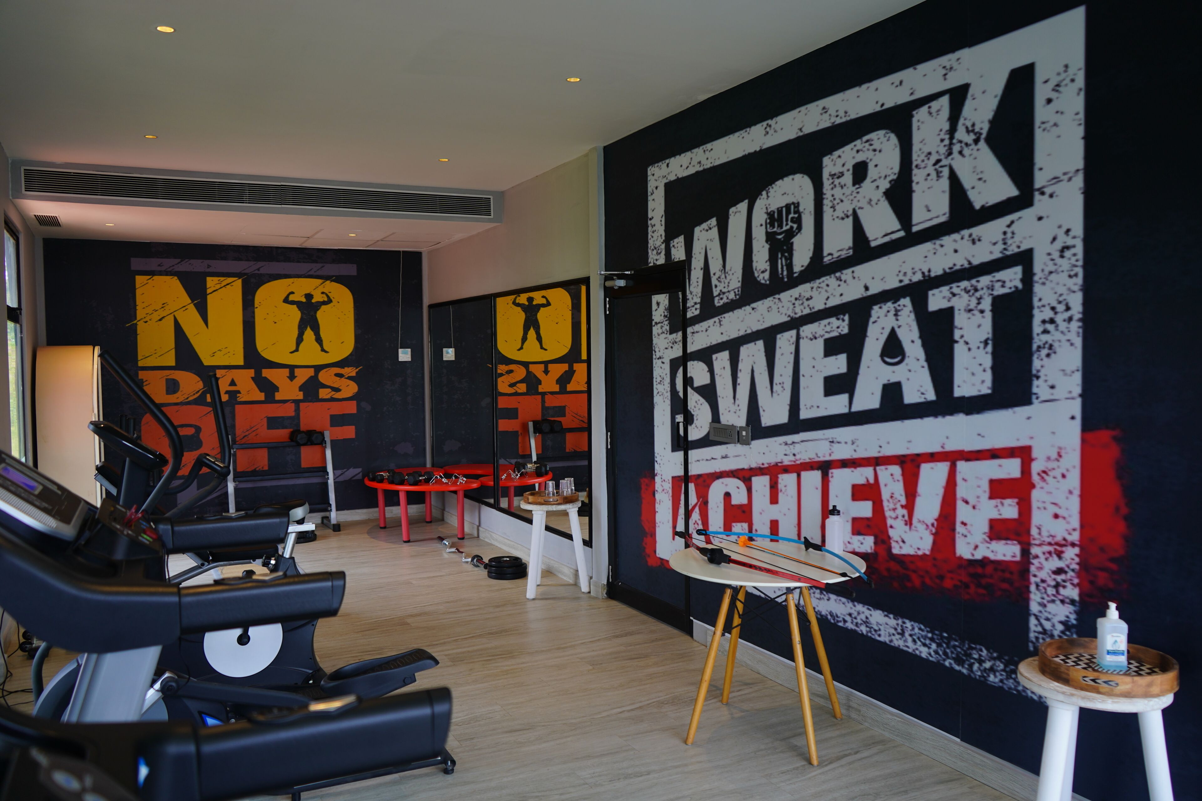 A gym with exercise equipment, motivational wall art, and a small stool with a bottle.
