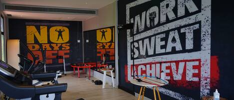 A gym with exercise equipment, motivational wall art, and a small stool with a bottle.