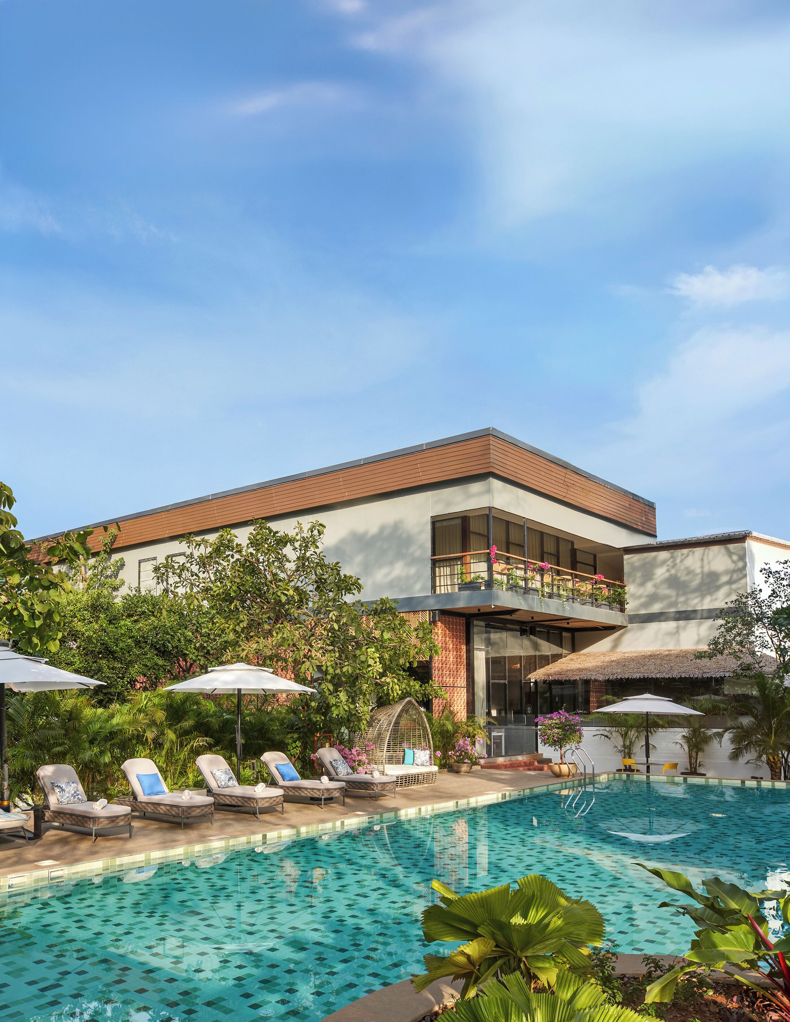 A modern hotel with a swimming pool, lounge chairs, and lush greenery.
