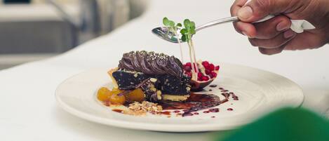 A dessert on a white plate with a spoon, garnished with green leaves and berries.