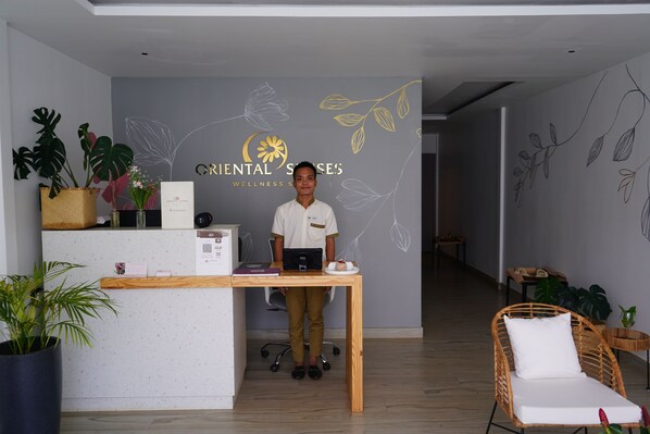 Un comptoir d’accueil orné d’un logo, agrémenté d’une plante, d’un fauteuil en osier et d’une table en bois.