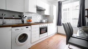 Une cuisine moderne avec des meubles blancs, un lave-linge Bosch, un four encastré et un coin repas comprenant une table et des chaises.