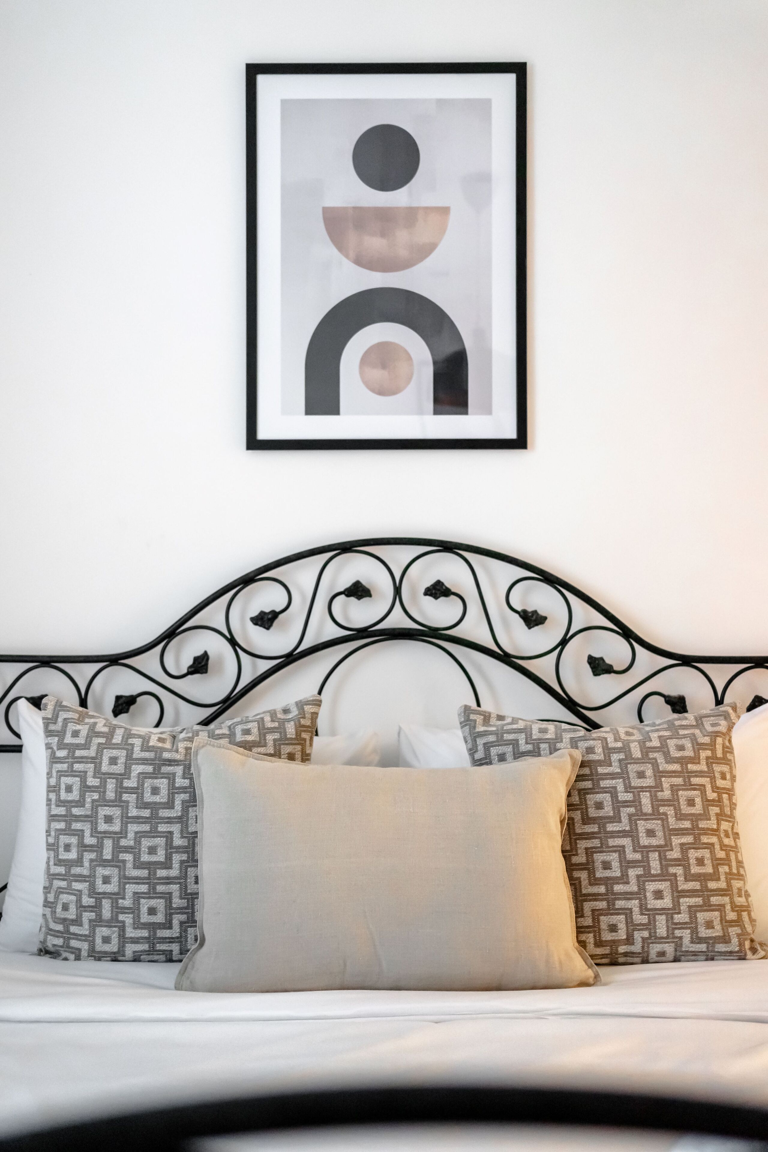 A neatly made bed with a black metal headboard, patterned pillows, and a framed abstract artwork on the wall.