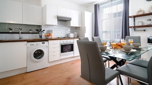 Une cuisine moderne avec des meubles blancs, un lave-linge encastré et un coin repas comprenant une table et des chaises en verre.