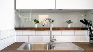 Une cuisine dotée d’un évier en acier inoxydable, d’un plan de travail en bois, d’un crédence carrelée de couleur blanche et de plantes en pot.