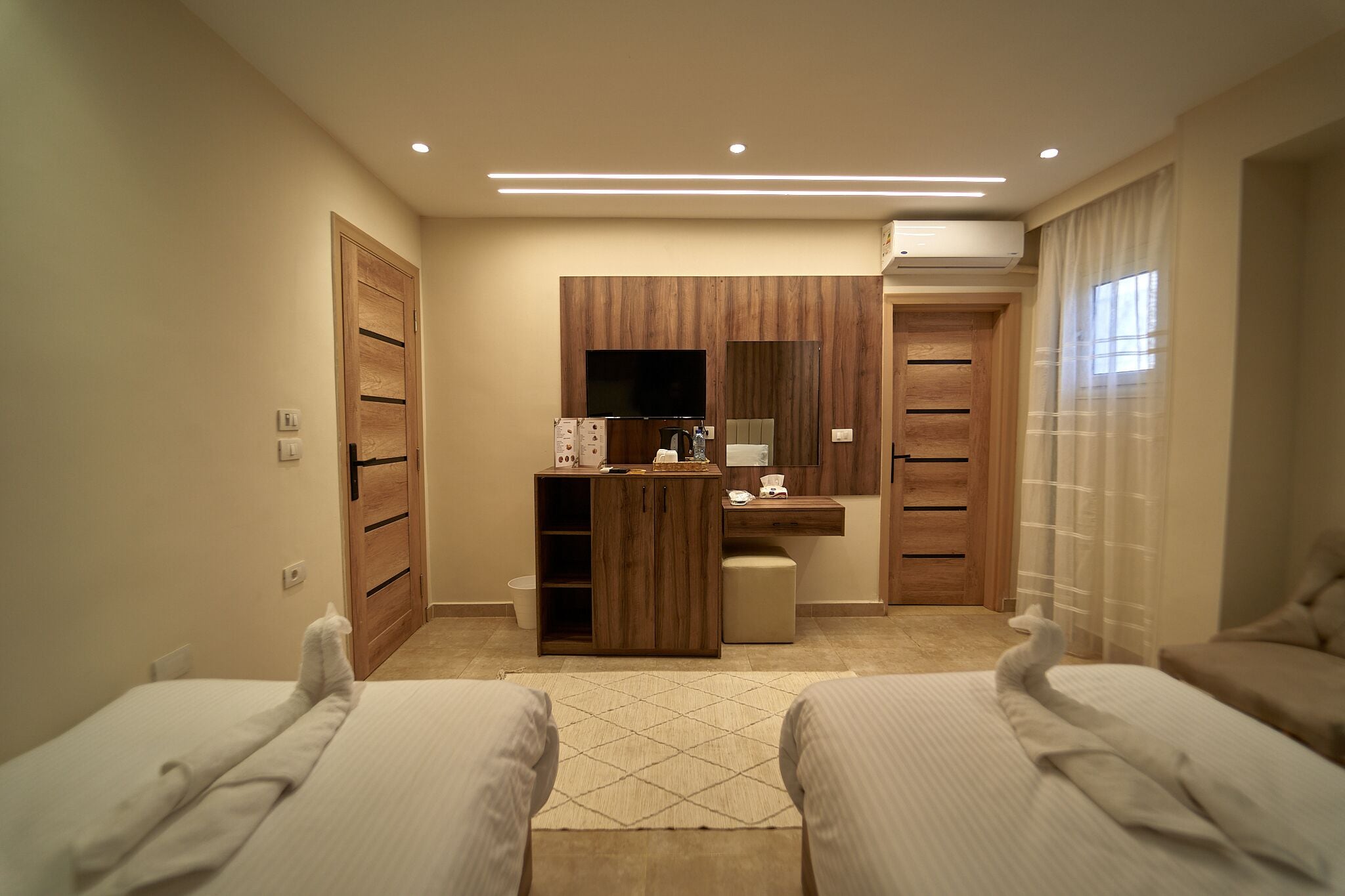 Une chambre d’hôtel avec deux lits, une armoire en bois, un bureau avec un miroir et une petite kitchenette.