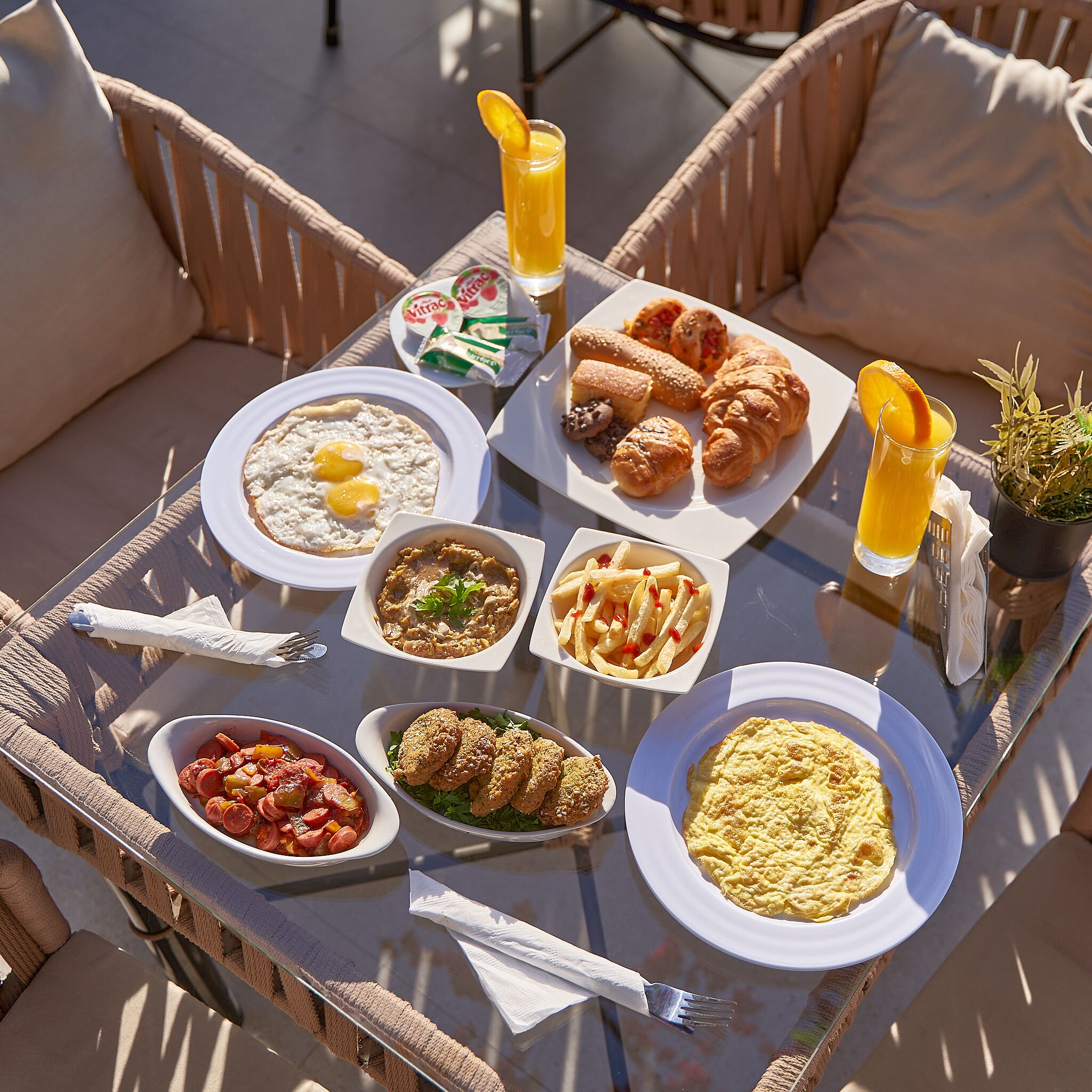 A breakfast tray with various dishes including eggs, croissants, and a fruit drink on an outdoor table.