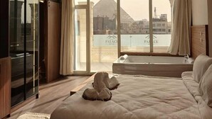 Habitación de hotel moderna con una cama grande, cabina de ducha de vidrio y vista a una pirámide.