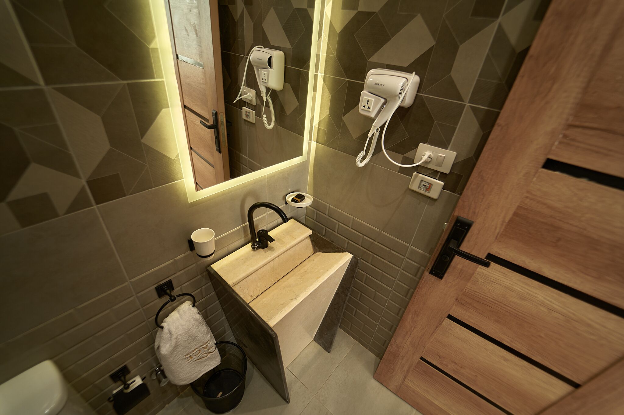 A modern bathroom with a wooden vanity, a sink, a mirror, and two hair dryers mounted on the wall.