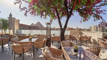 Relax in the shaded outdoor seating area with wicker furniture and glass tables, offering a view of the nearby pyramid.