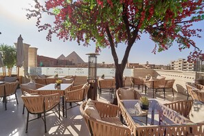 An outdoor seating area with wicker furniture, a central table, and a decorative tree with pink flowers.