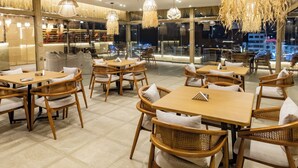 Un restaurante con mobiliario de mimbre, lámparas colgantes y vistas a la ciudad de noche.