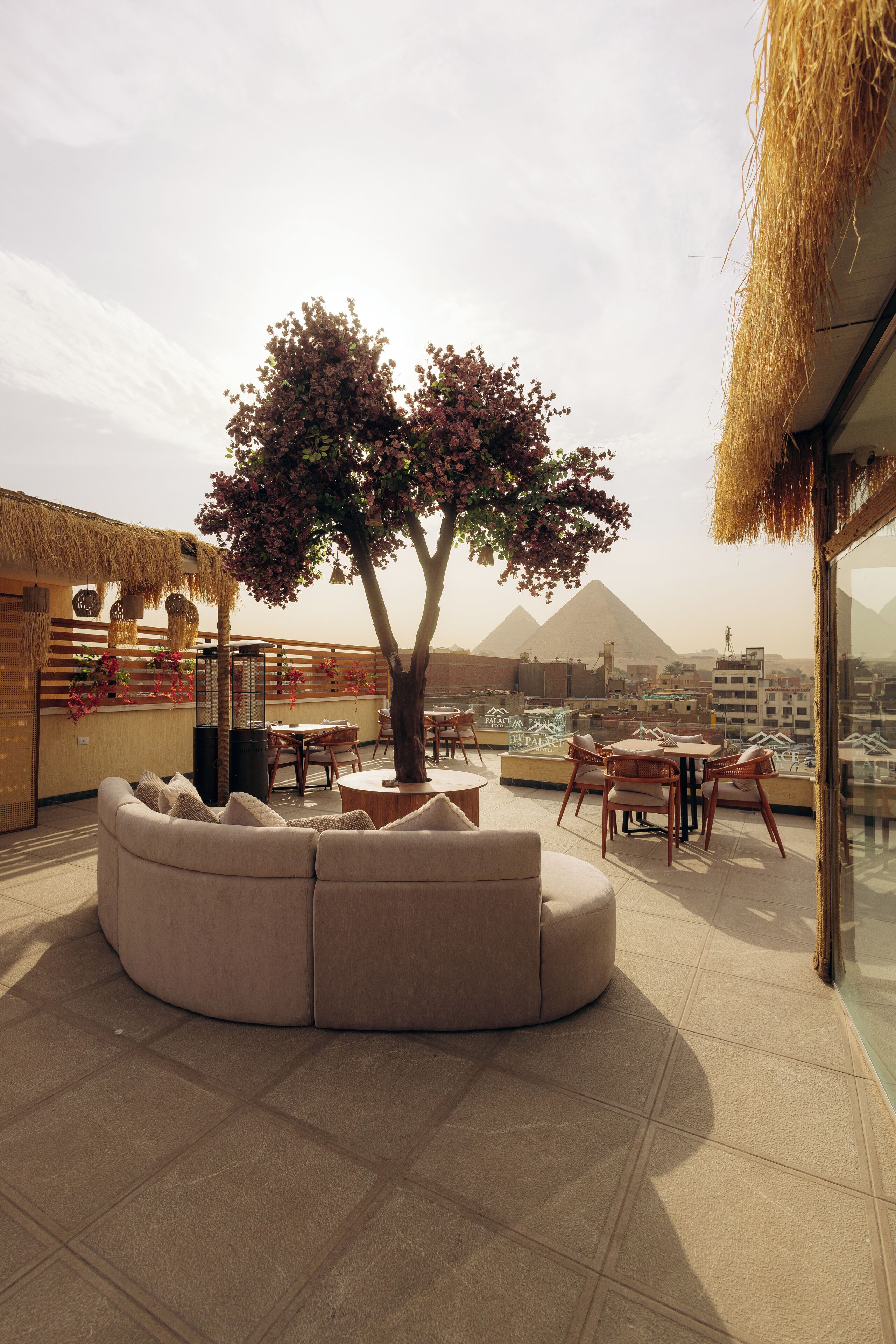 Un salon sur le toit, doté d’un espace salon avec des sièges confortables, une table et des chaises, offrant une vue sur le paysage urbain avec des pyramides en arrière-plan.
