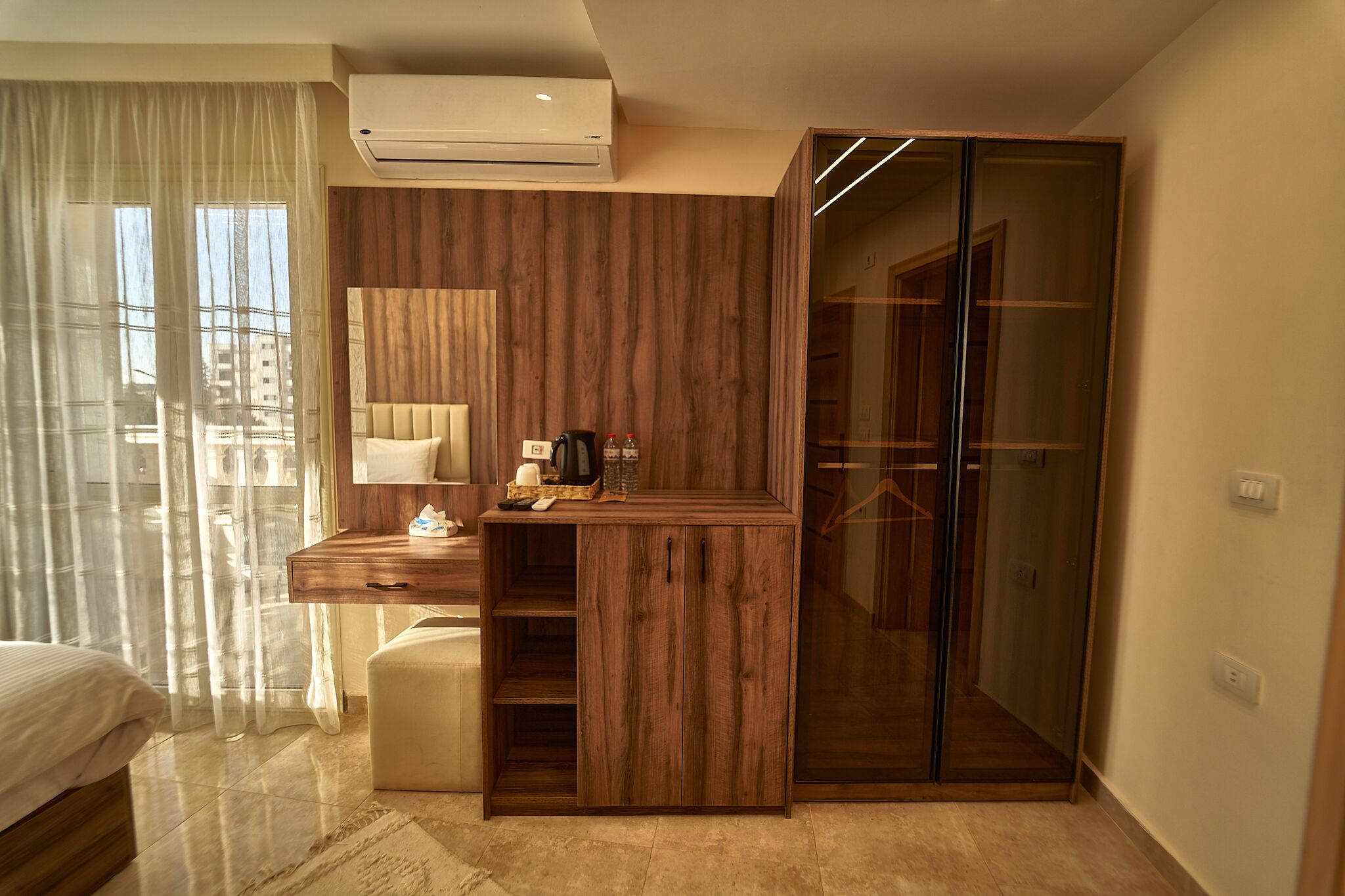 A modern hotel room with a wooden vanity, a bed, and a glass closet.