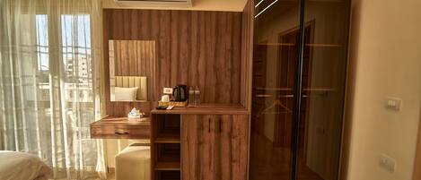 A modern hotel room with a wooden vanity, a bed, and a glass closet.