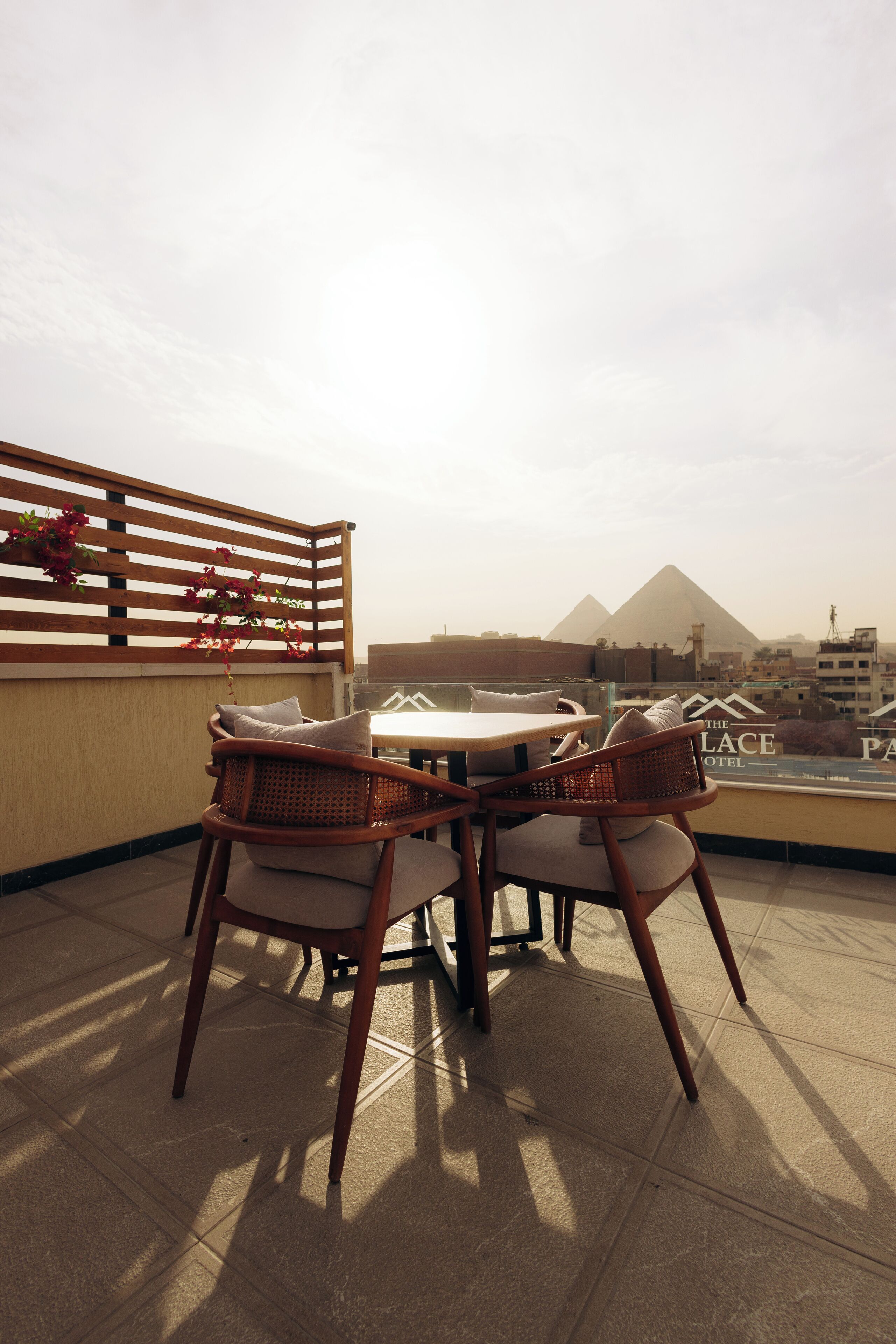 Una terraza con sillas de mimbre y una mesa, con vista a un paisaje urbano y pirámides.