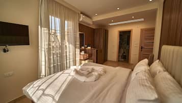 A modern bedroom with a large bed, a TV mounted on the wall, and a walk-in closet.