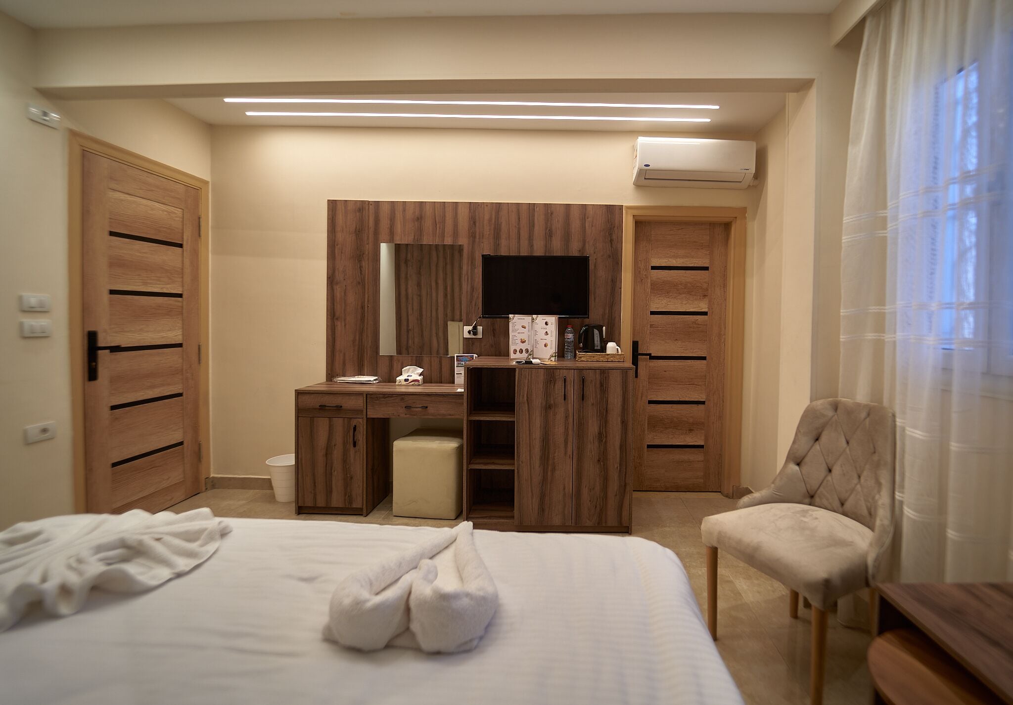A hotel room with a bed, a desk with a mirror, a chair, and an air conditioning unit.