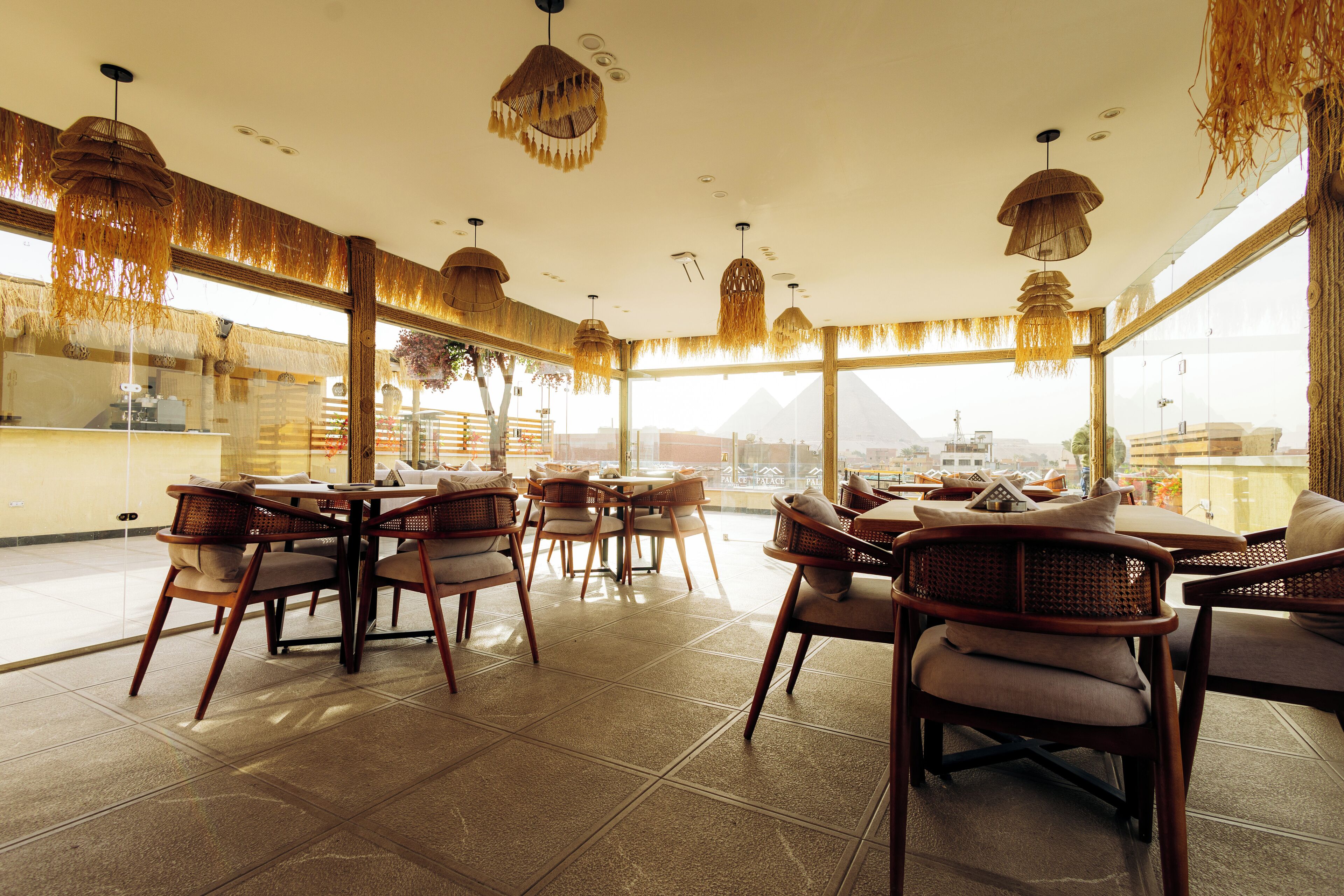 A restaurant with wicker furniture and hanging lights, large windows, and a view of pyramids.