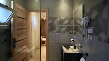 Un baño moderno con mampara de vidrio, tocador de madera, lavamanos y zona de ducha.