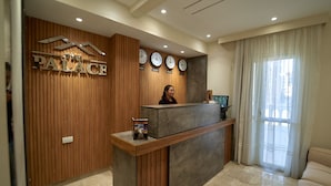 Un mostrador de recepción de hotel con un panel de pared de madera, un letrero que dice "The Palace" y relojes en la pared.