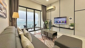 A modern living room with a sofa, a flat-screen TV, and a balcony with a view of the sea. - Country Garden Danga Bay By Stayrene (Johor Bahru)