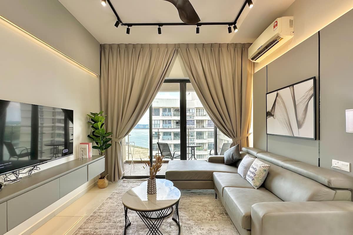 A modern living room with a flat-screen TV, a sofa, a coffee table, and a view of a building through large windows.