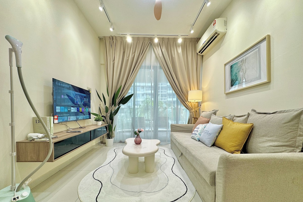 A modern living room with a flat-screen TV, a sofa with cushions, a coffee table, and a large window with curtains.