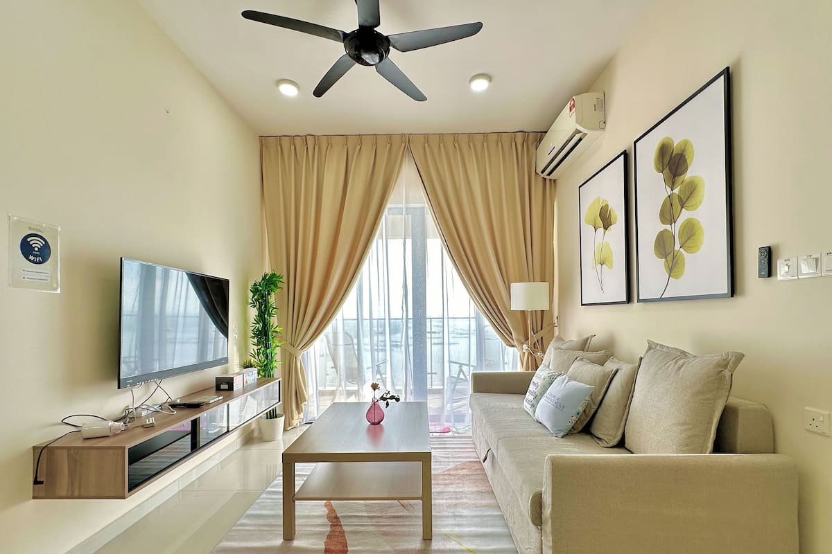A modern living room with a flat-screen TV, a ceiling fan, a sofa, a coffee table, and a large window with curtains.
