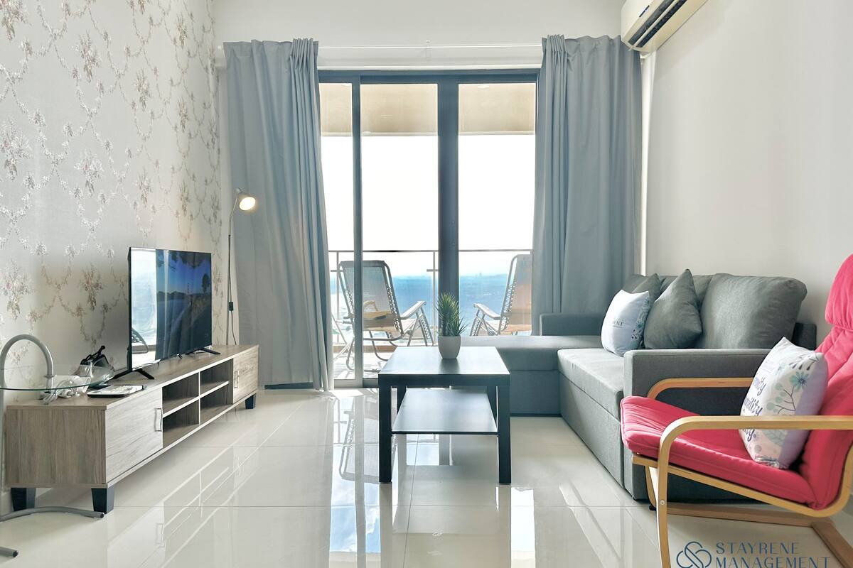 A modern living room with a flat-screen TV, a sofa, a dining table, and a balcony with a view.