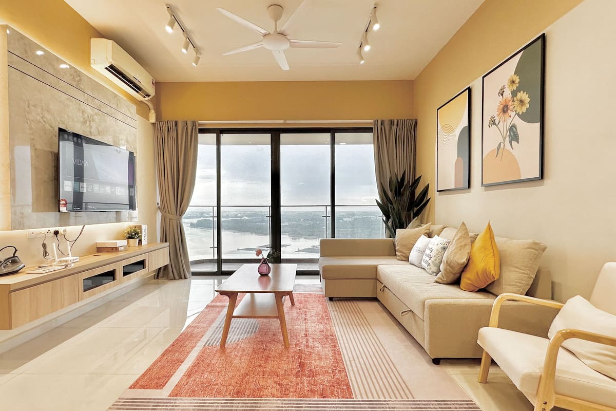 A modern living room with a large TV, a sofa, a coffee table, and a view of the city through large windows.