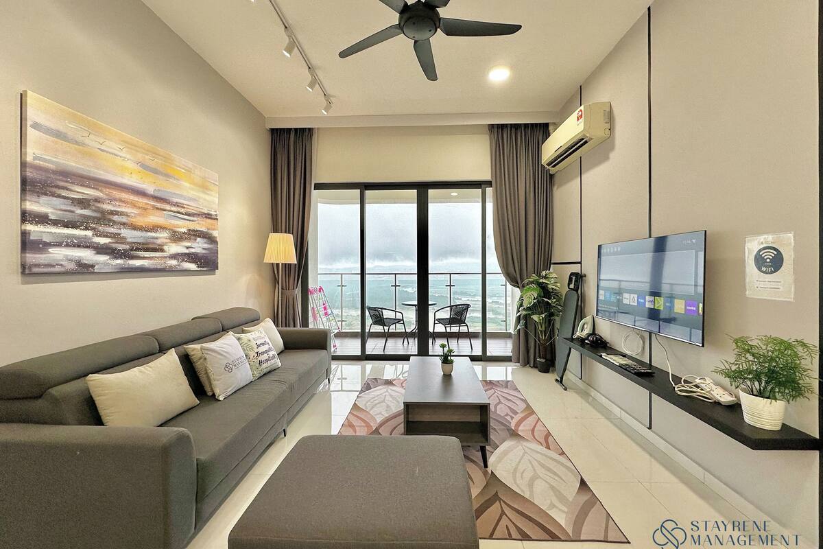 A modern living room with a sofa, a coffee table, a TV, and a balcony with a view of the ocean.