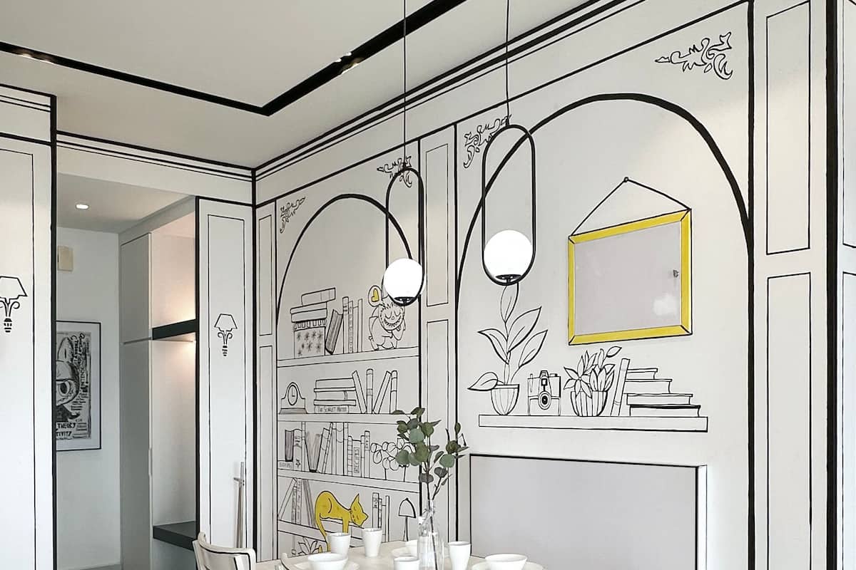 A dining area with a white table and chairs, a vase with flowers, and wall art including a framed picture and shelves with books and decorative items.