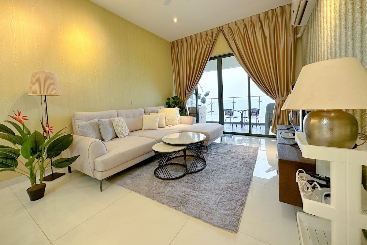 A modern living room with a sofa, coffee table, and a view of the sea through large windows.