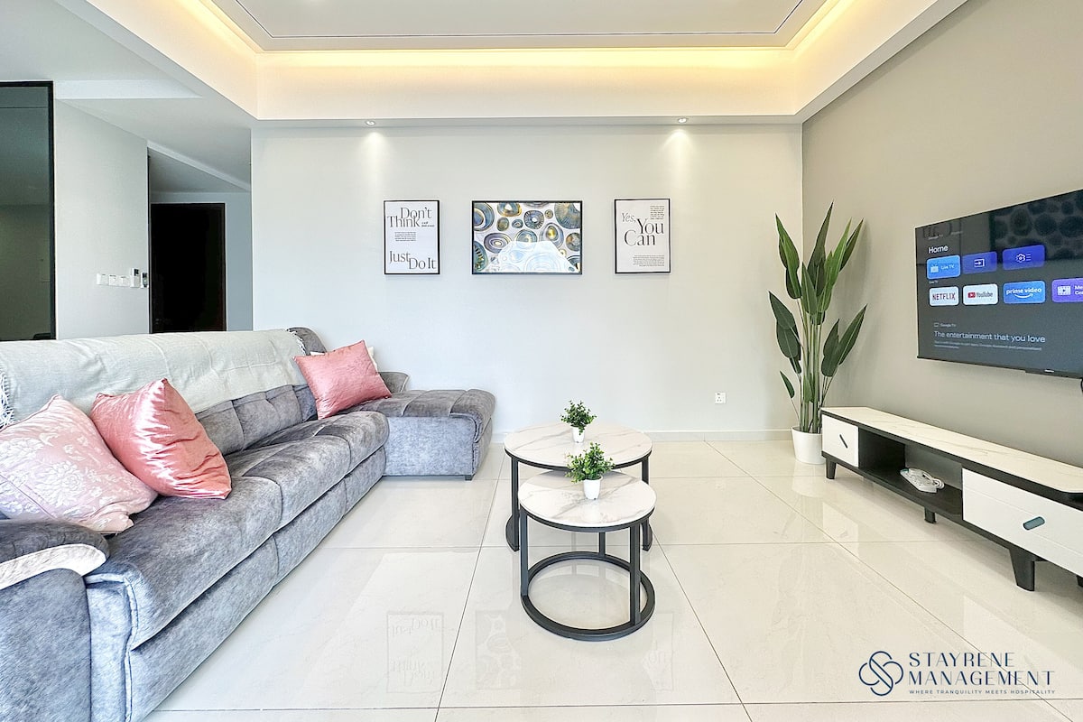 A modern living room with a grey sofa, a round coffee table, and a flat-screen TV mounted on the wall.