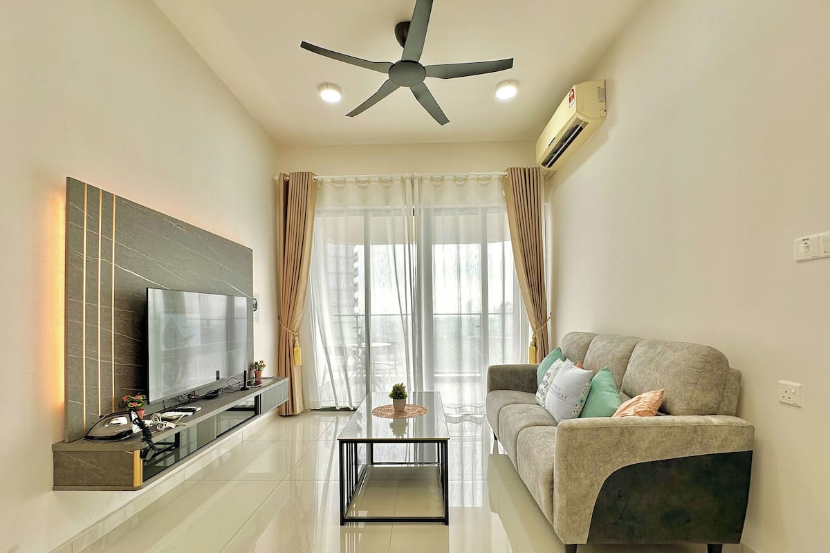 A modern living room with a flat-screen TV, a ceiling fan, and a sofa with cushions.
