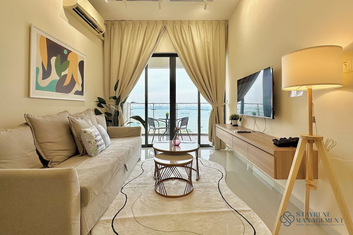A modern living room with a sofa, a coffee table, a TV, and a view of the sea.