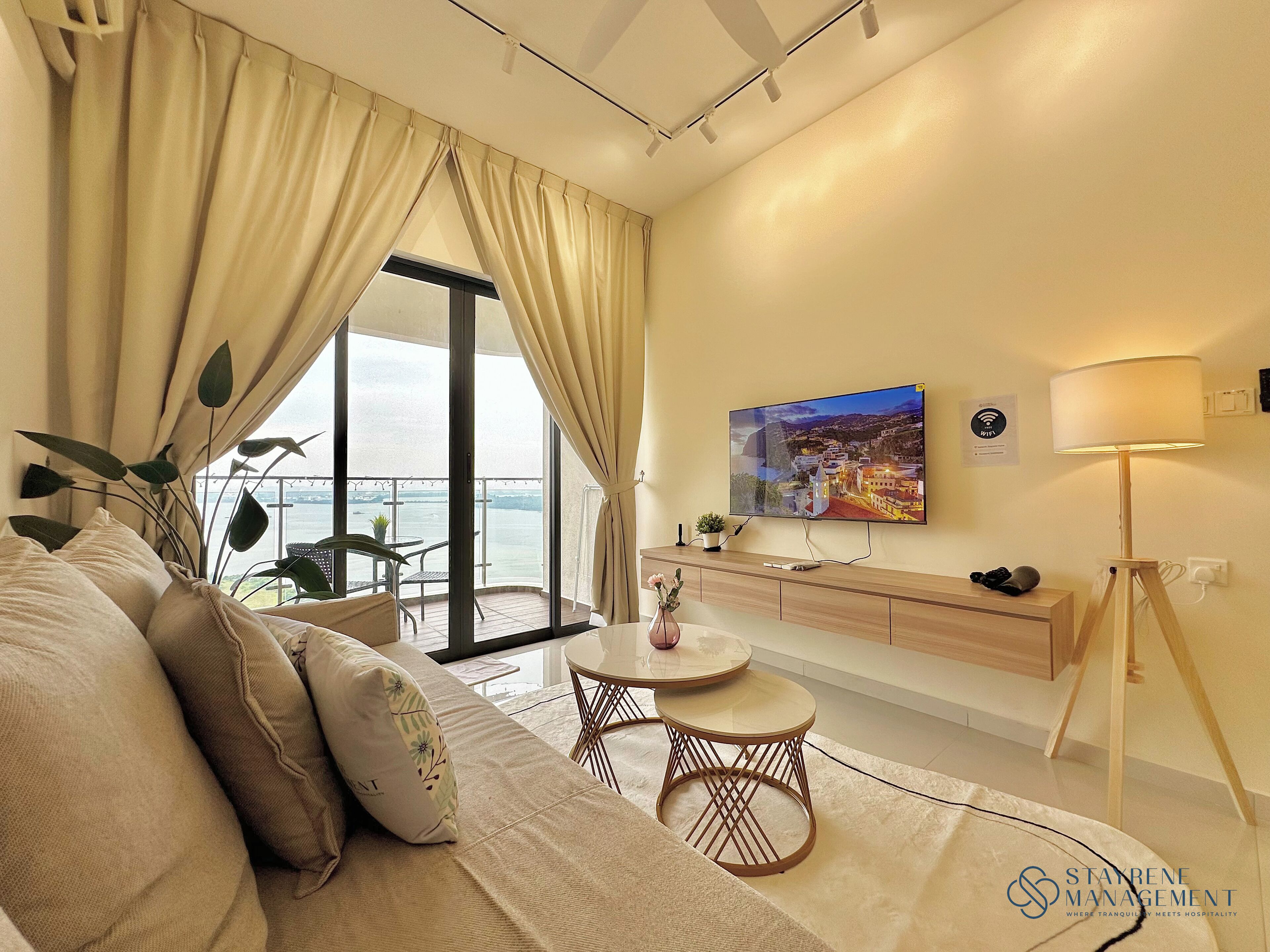 A modern hotel room with a large window, a sofa, a small round table, a TV, and a lamp.