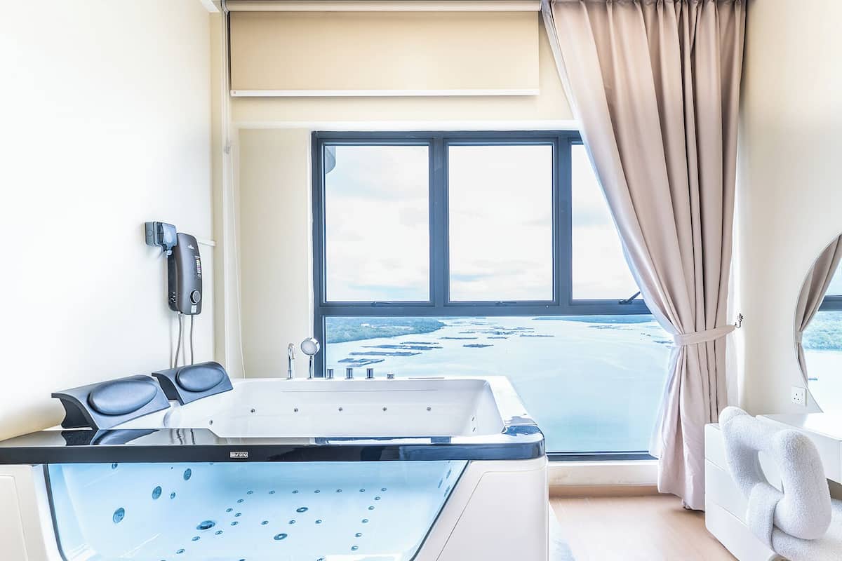 A spa room with a hot tub, a massage chair, a window with a view of the sea, and a towel rack.