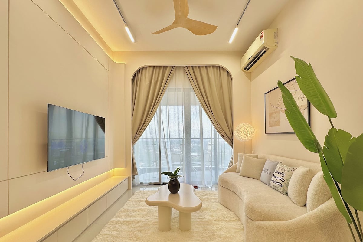 A modern living room with a flat-screen TV, a ceiling fan, and a large window with curtains.