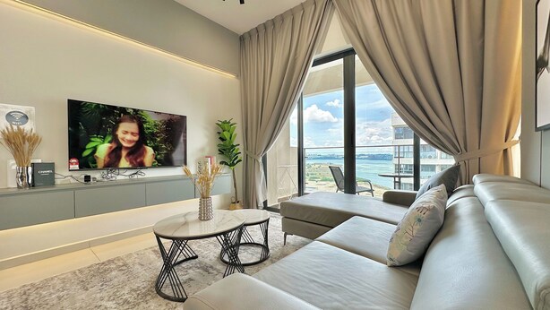 A modern living room with a flat-screen TV, a sofa, a coffee table, and a view of the sea. - Country Garden Danga Bay By Stayrene (Johor Bahru)