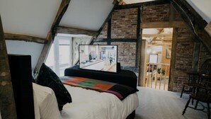 A loft-style bedroom with a bed, a television, and a view of a kitchen area. - Urban Lofts, Melksham - Butler (Melksham)